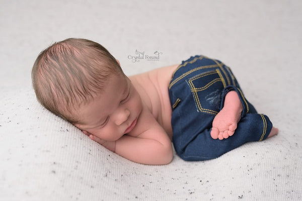 Newborn baby wrapped in denim fabric on a light gray background